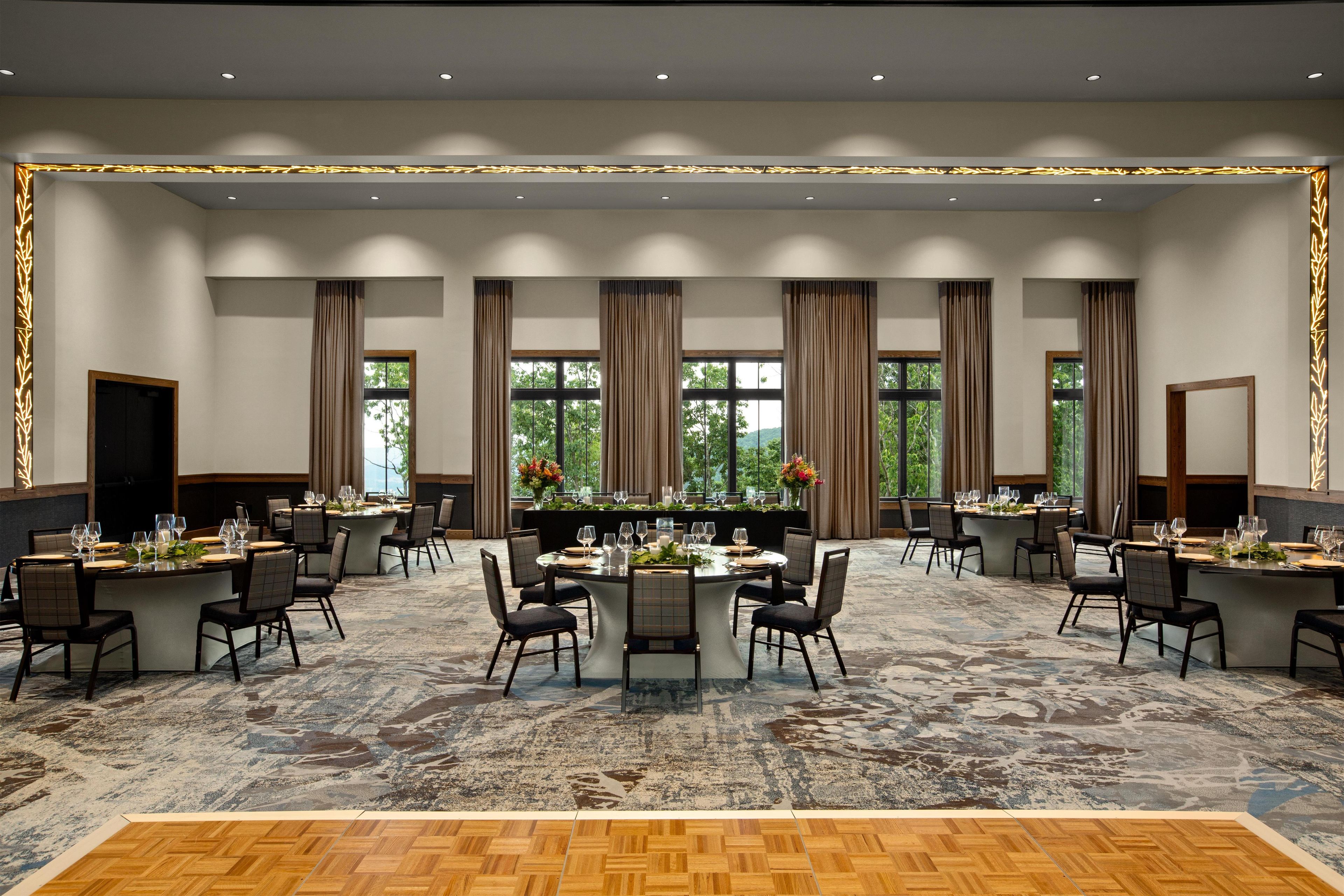 A conference room with multiple tables, chairs, and large windows with curtains.