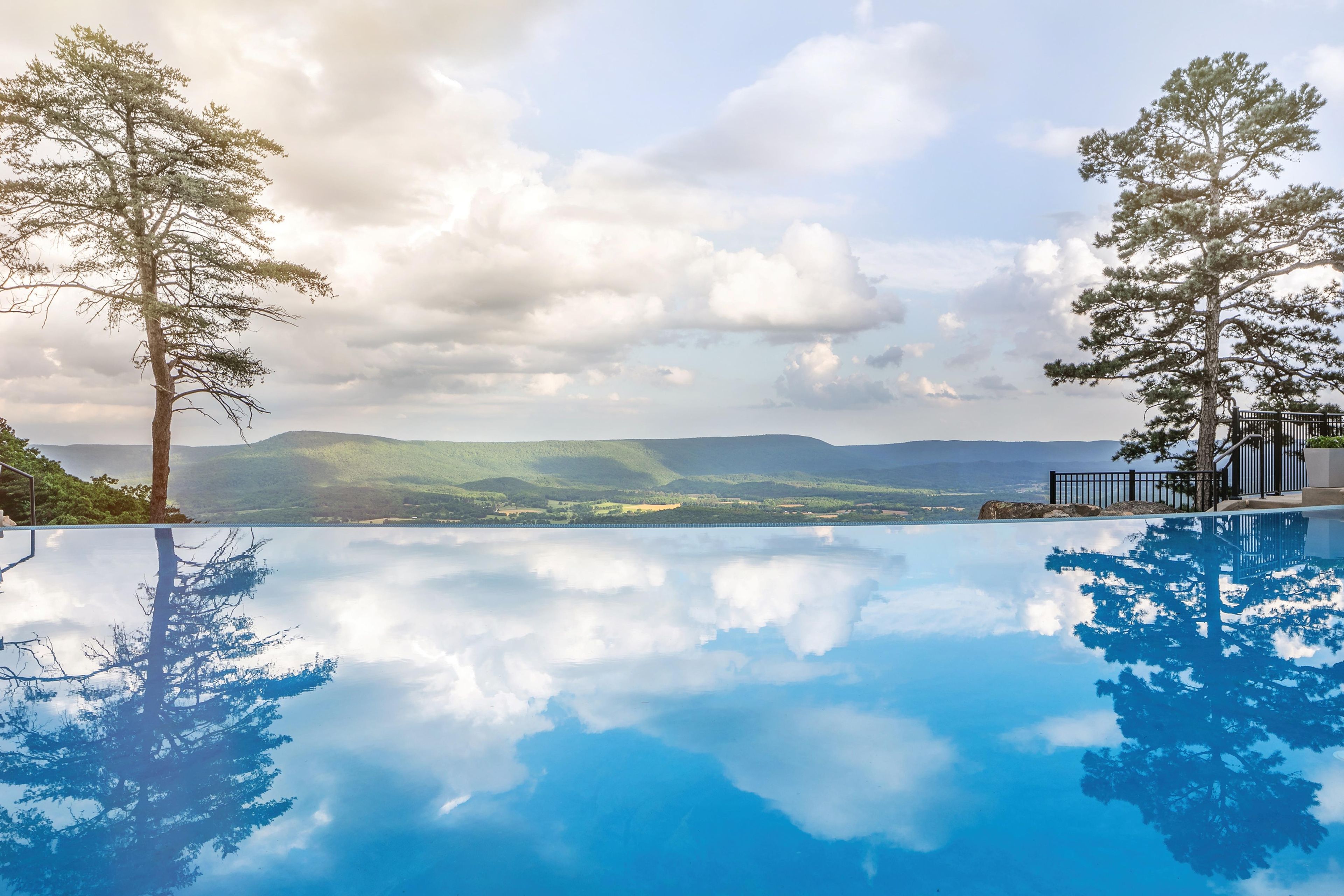 Vista clara de una piscina con reflejos de árboles y montañas.