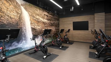 A gym with stationary bikes, a large wall mural of a waterfall, and wooden paneling.