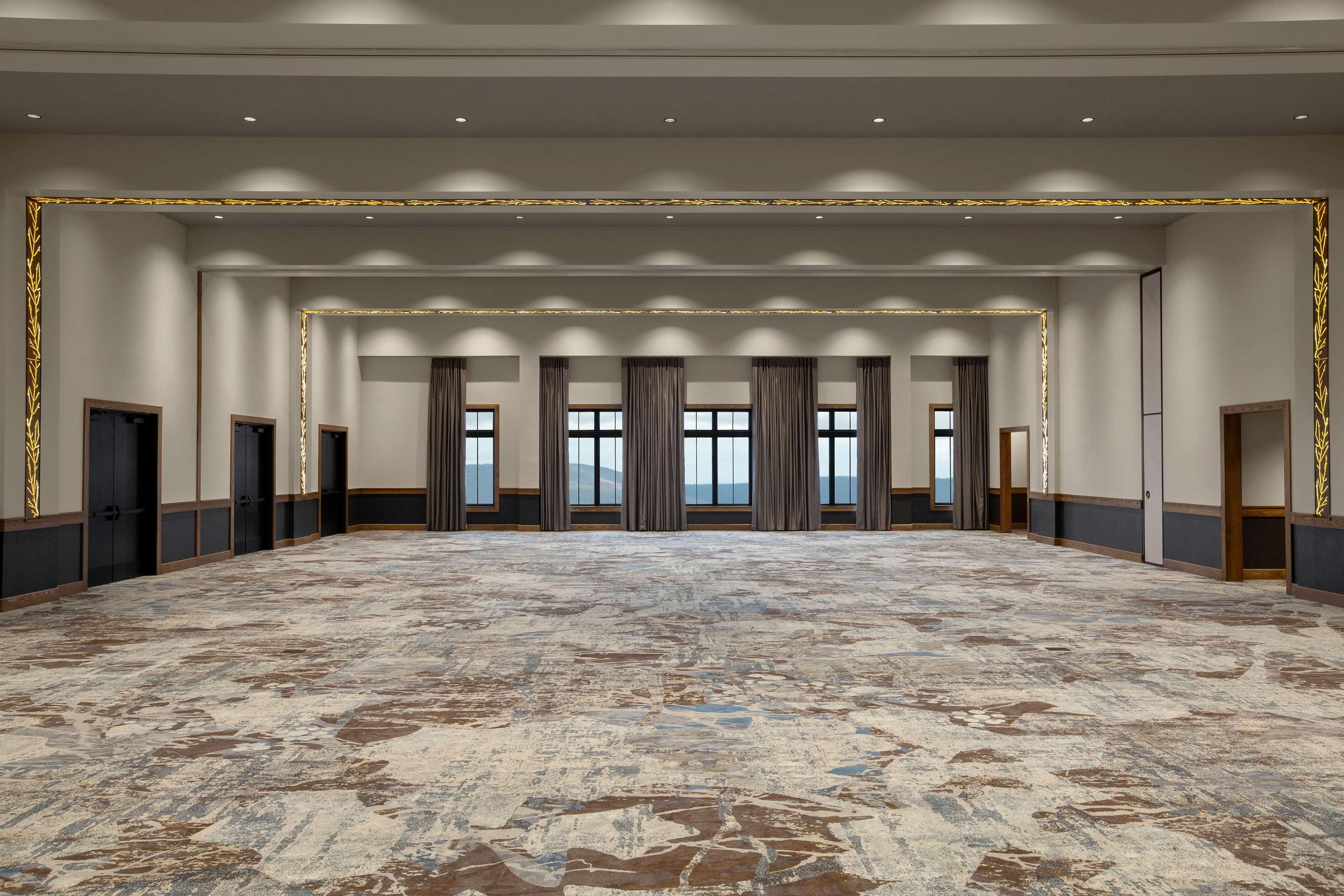 A spacious conference room with a patterned carpet, large windows with curtains, and a view of the outdoors.