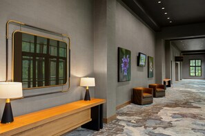 En hotelllobby med en bänk, en spegel, en lampa, inramade konstverk och ett mattbeklätt golv.