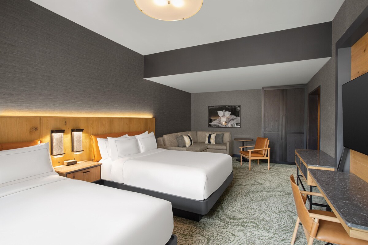 Ett modernt hotellrum med två sängar, en soffa, ett skrivbord och en stol.
