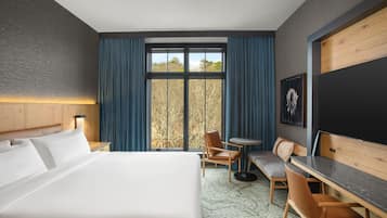 A hotel room with a large bed, a desk, a chair, a small table, and a window with curtains.