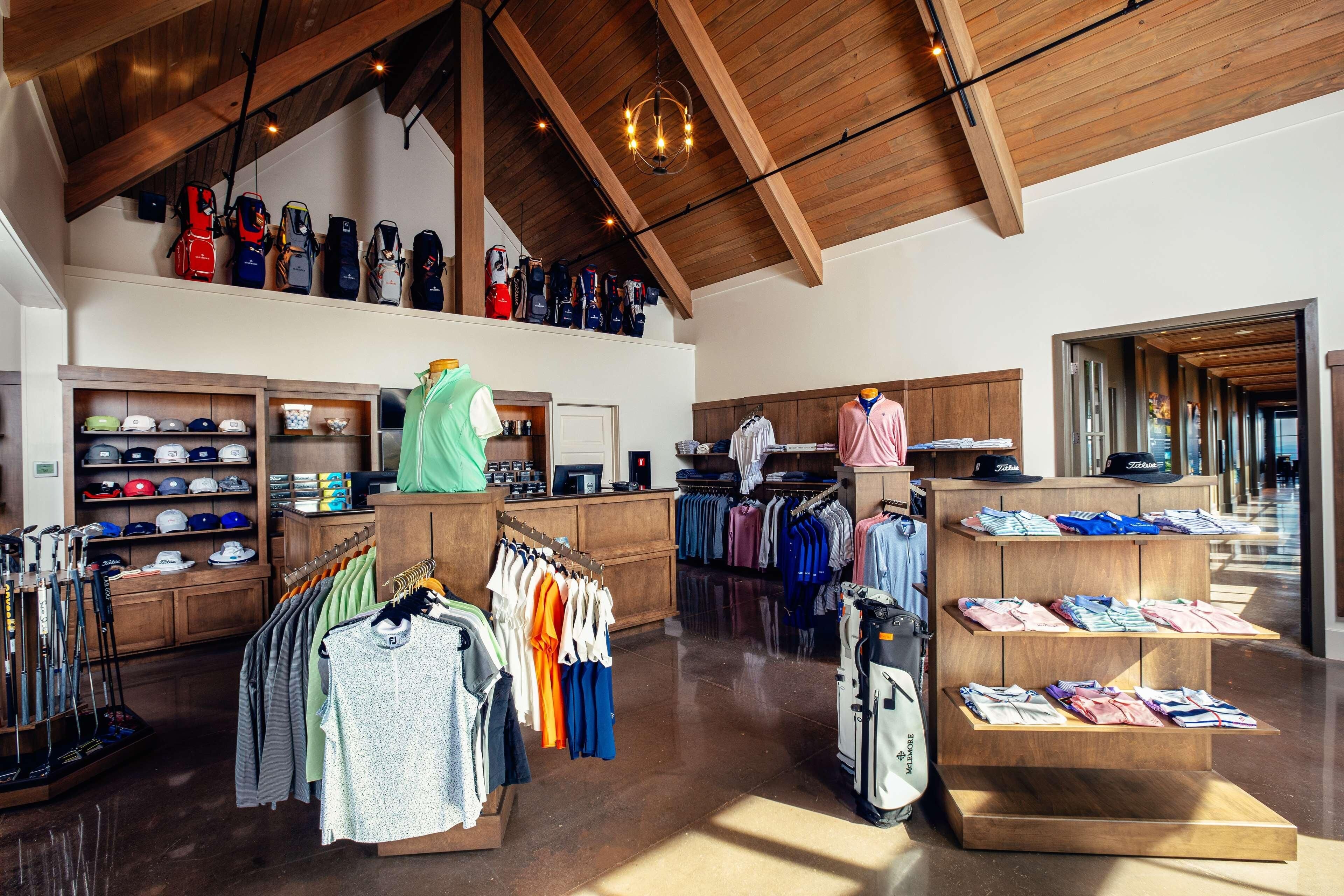 A spacious retail store with wooden beams on the ceiling, racks of clothing, and shelves of hats and caps.