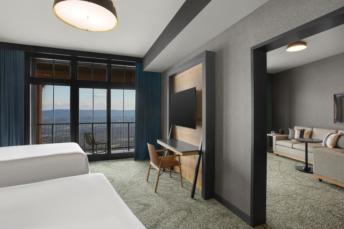 Une chambre d’hôtel avec une grande fenêtre, un bureau, une chaise, un canapé et un téléviseur.