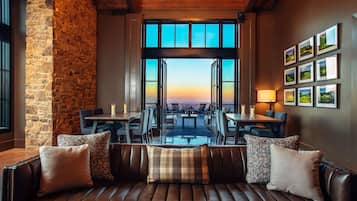 A cozy seating area with a stone wall and a view of the sunset through open doors.
