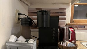 Une machine à café, une bouilloire rouge, un récipient portant l’inscription « bienvenue » et un panier rempli d’ustensiles, le tout posé sur un plan de travail de cuisine.