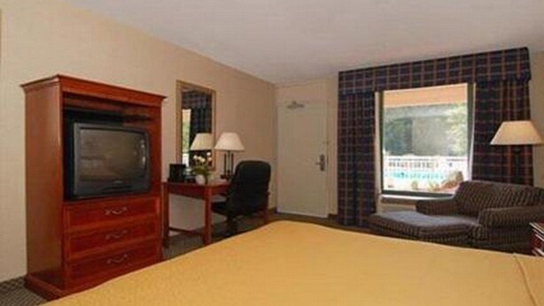A hotel room with a bed, a television, a desk with a lamp, a chair, and a window with curtains. - Travelodge by Wyndham Suffolk (Suffolk)