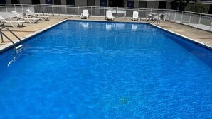 A rectangular swimming pool with clear blue water, surrounded by white lounge chairs and a white fence. - Travelodge by Wyndham Suffolk (Suffolk)