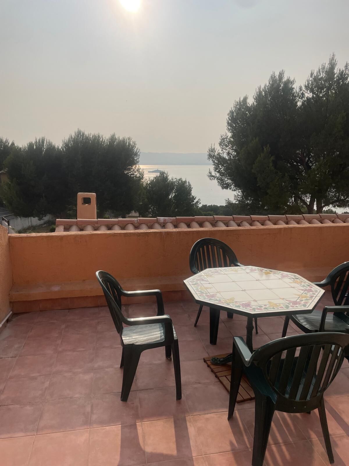 A terrace with a tiled table and chairs, overlooking a body of water and trees.