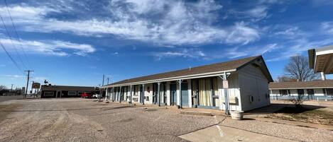 A motel with a row of single-story rooms, a parking lot, and a clear blue sky.