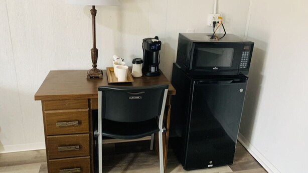 A compact kitchenette with a microwave, coffee maker, and a small table with cups and a lamp.