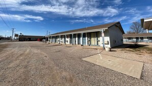A motel with a row of rooms, a parking lot, and a building in the background.