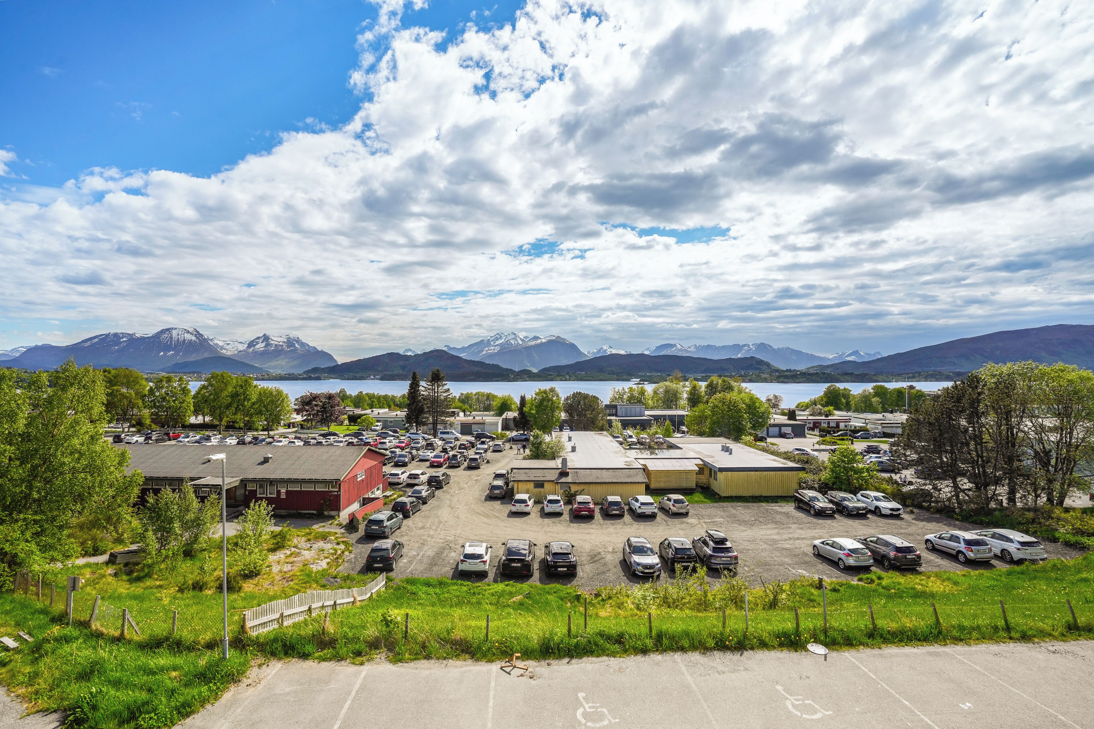 A parking lot with cars, a building with a red roof, and mountains in the background.