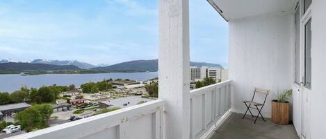 A balcony with a view of a lake and mountains, a wooden chair, and a potted plant.