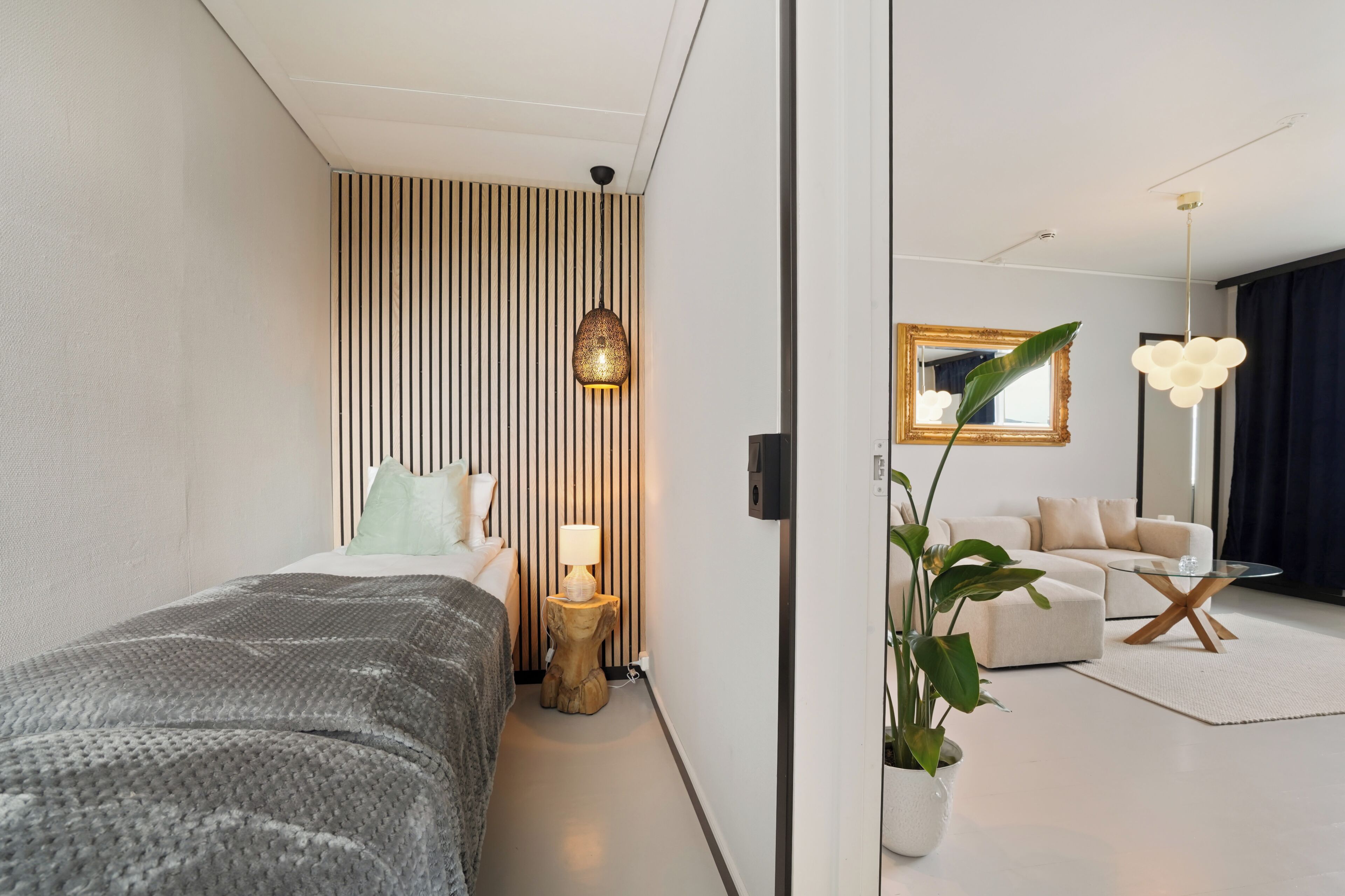 Una habitación de hotel moderna con cama, mesita de noche, lámpara y vista al área de estar.