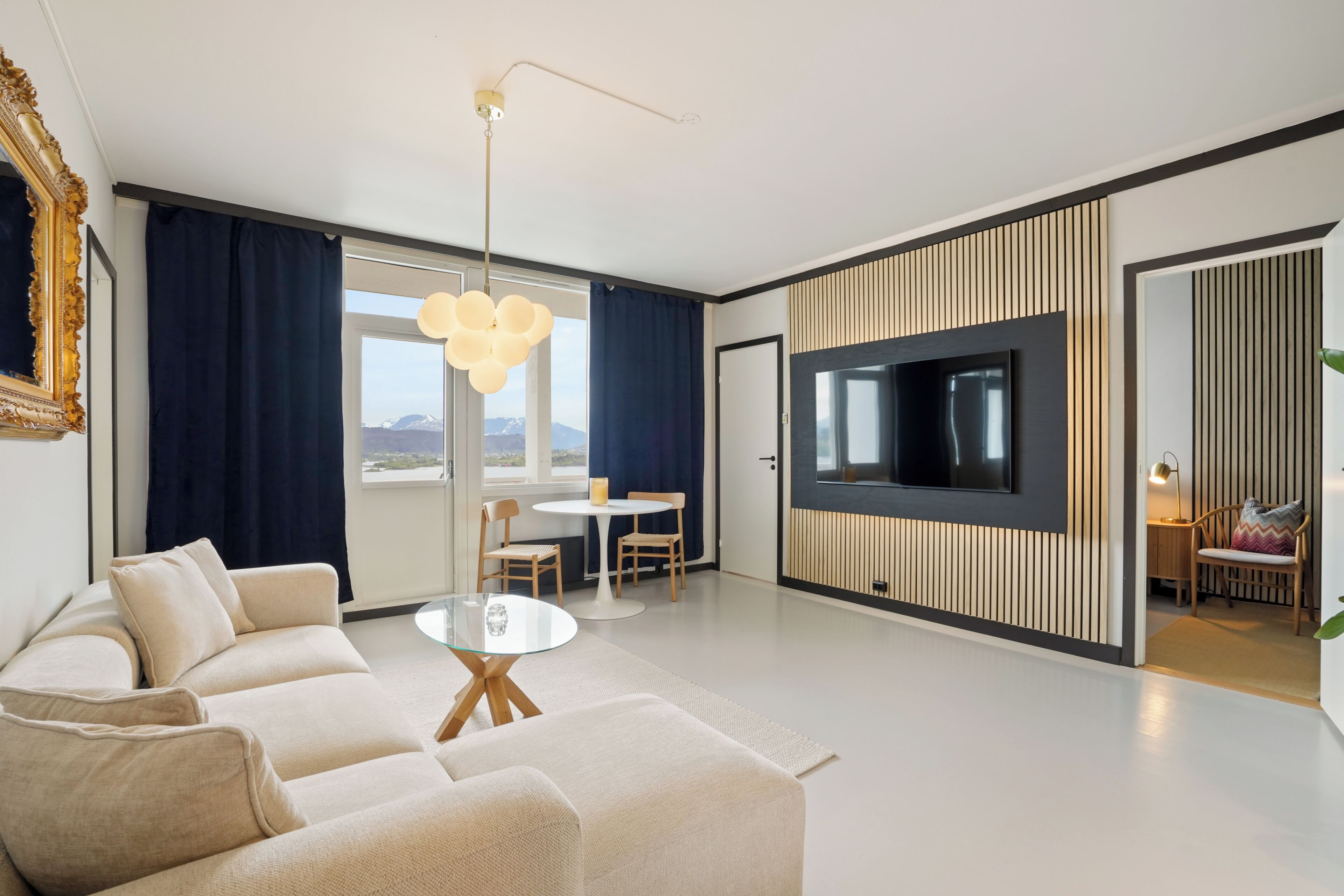A modern living room with a sofa, a round coffee table, a TV mounted on a wall, and a dining area with a table and chairs.