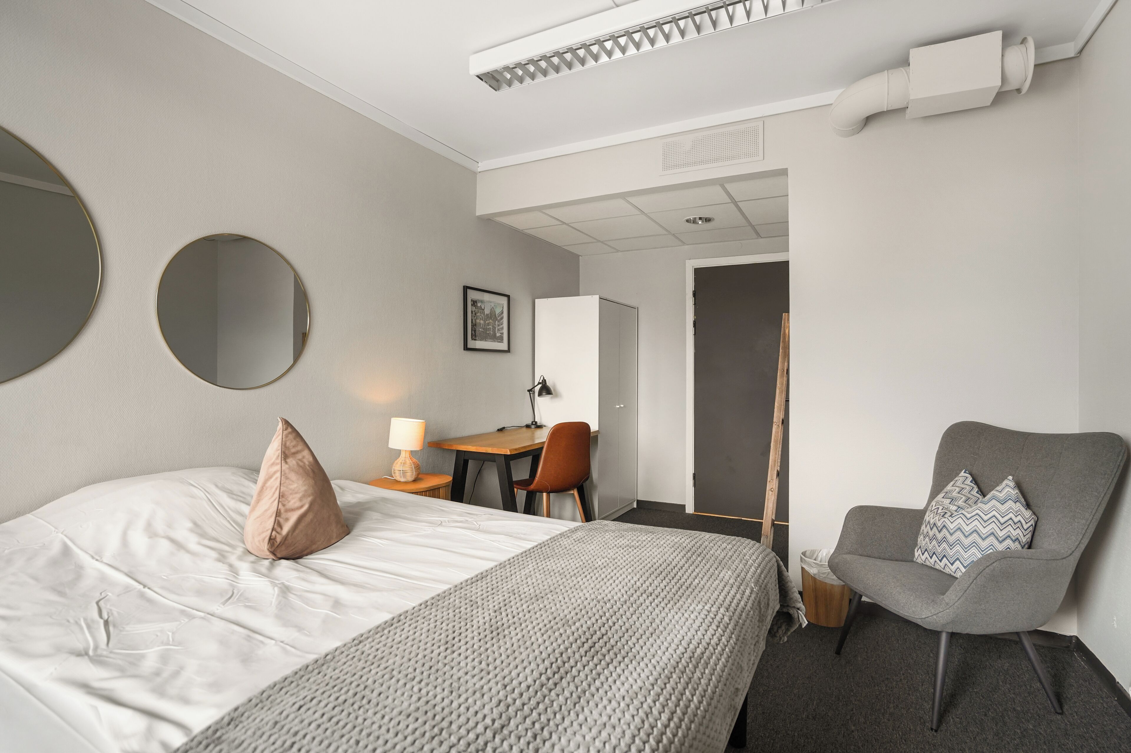 A hotel room with a bed, a desk, a chair, and a large mirror.