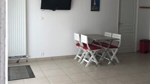 Un coin repas avec une table et des chaises, un téléviseur fixé au mur et un luminaire suspendu rouge.