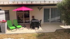 Une terrasse avec deux chaises vertes, une table et un parasol rose.