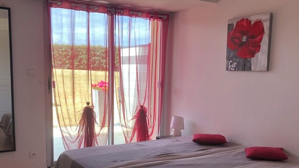 Une chambre avec deux lits, une grande fenêtre ornée de rideaux légers, un tableau représentant une fleur rouge et un sol carrelé.