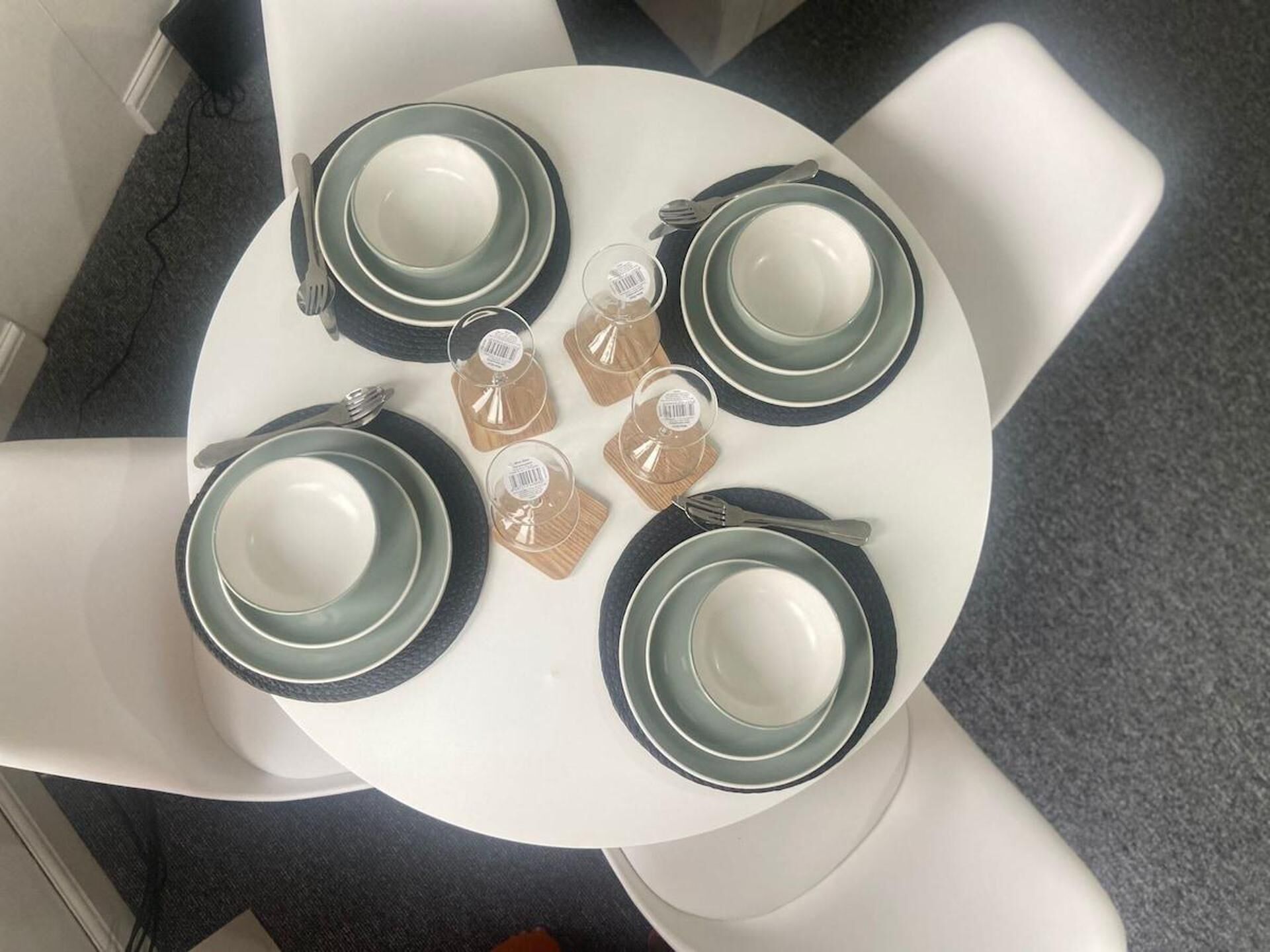 A round table with four plates and cutlery, surrounded by four white chairs.