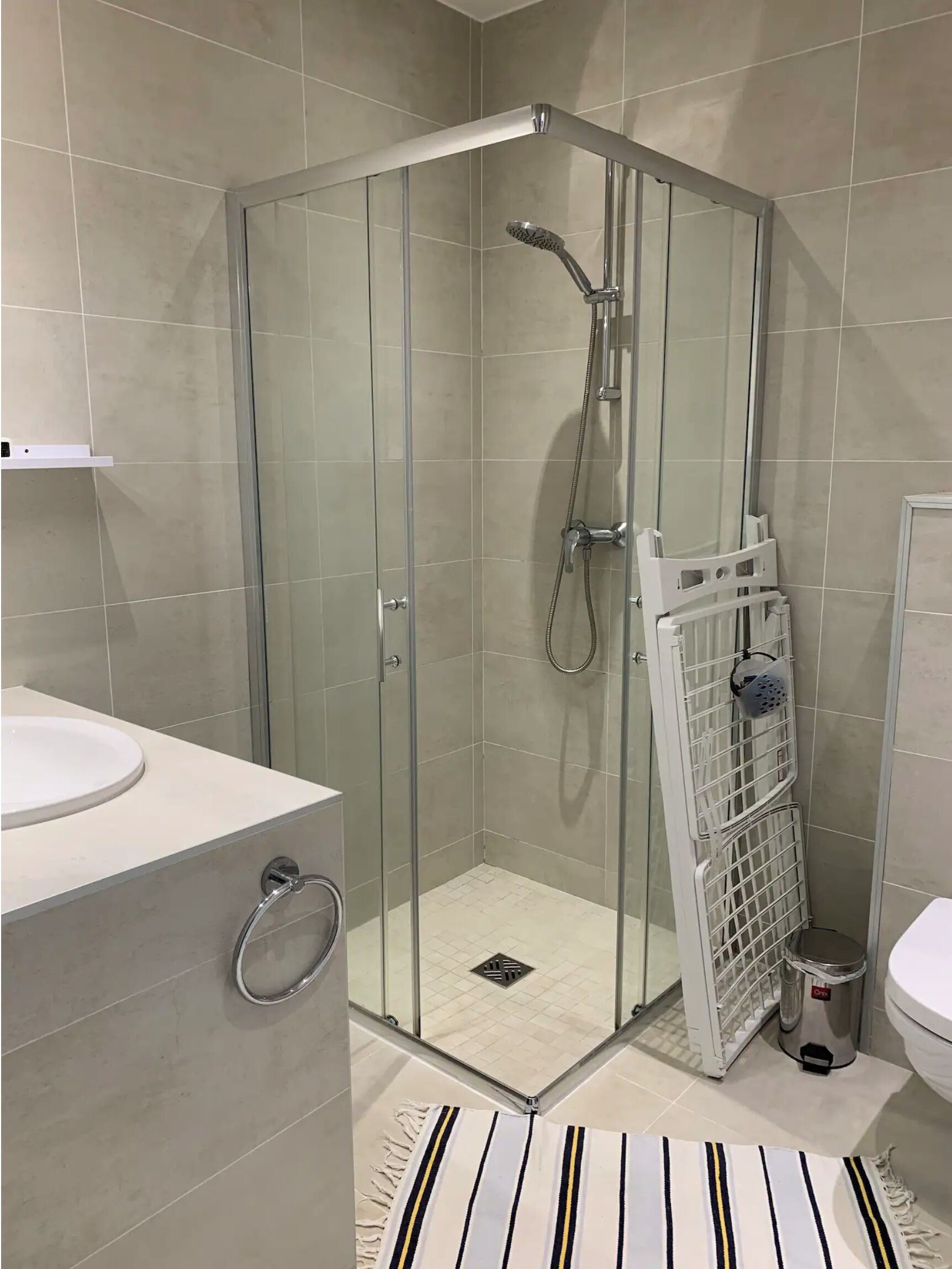 A modern bathroom with a glass-enclosed shower, a white sink, and a striped rug.
