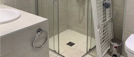 A modern bathroom with a glass-enclosed shower, a white sink, and a striped rug.