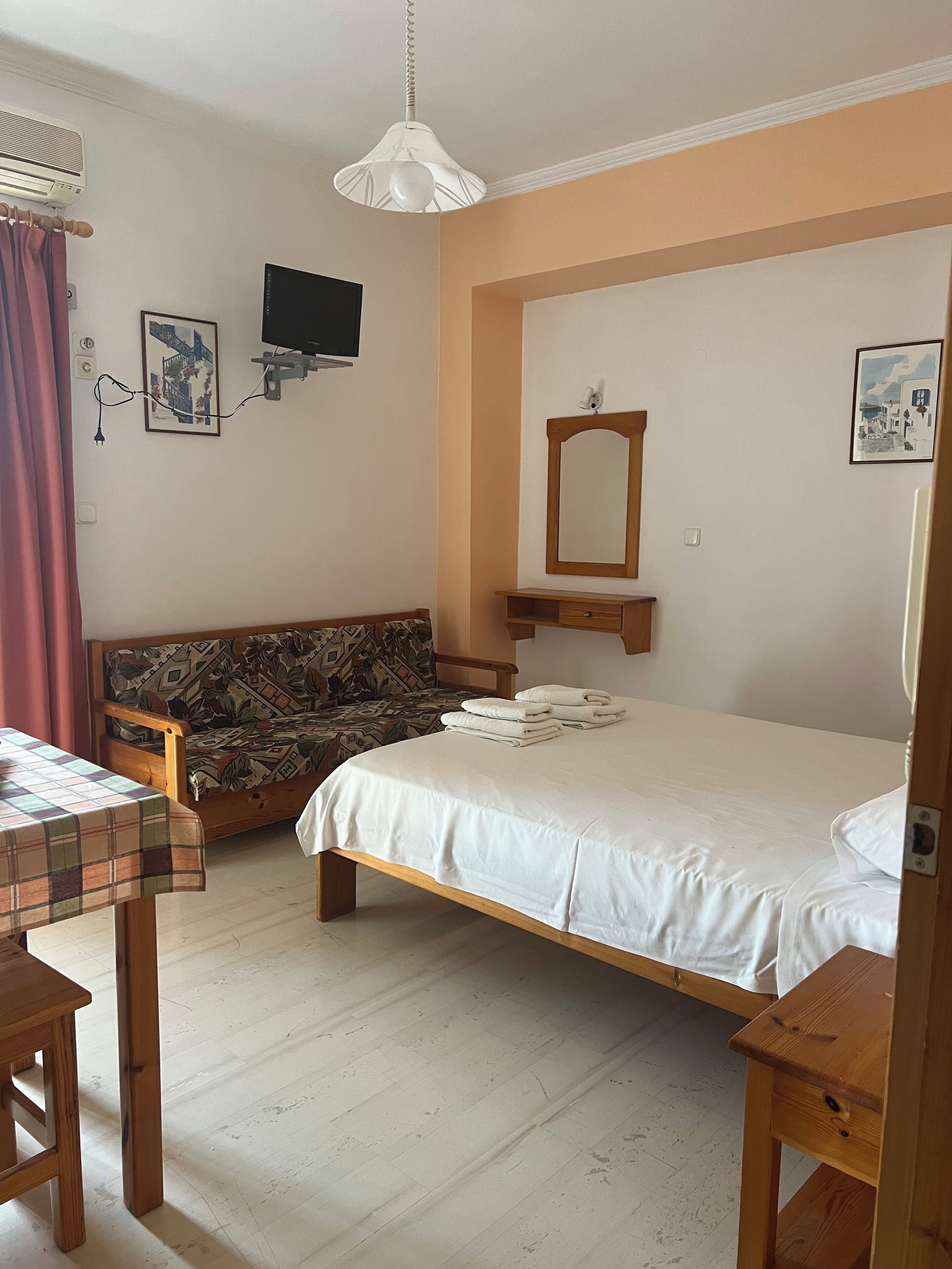 Un dormitorio con una cama, un banco de madera, una mesa, un televisor y un espejo.