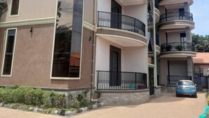 A multi-story residential building with balconies, a car parked in front, and a paved driveway. - Eden Homes (Kampala)