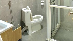 A modern bathroom with a toilet, a glass shower enclosure, and a hand dryer mounted on the wall. - Eden Homes (Kampala)
