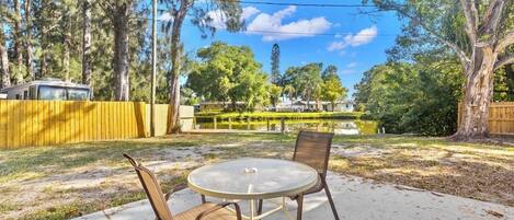 A backyard with a round table and chairs, surrounded by trees and a fence.