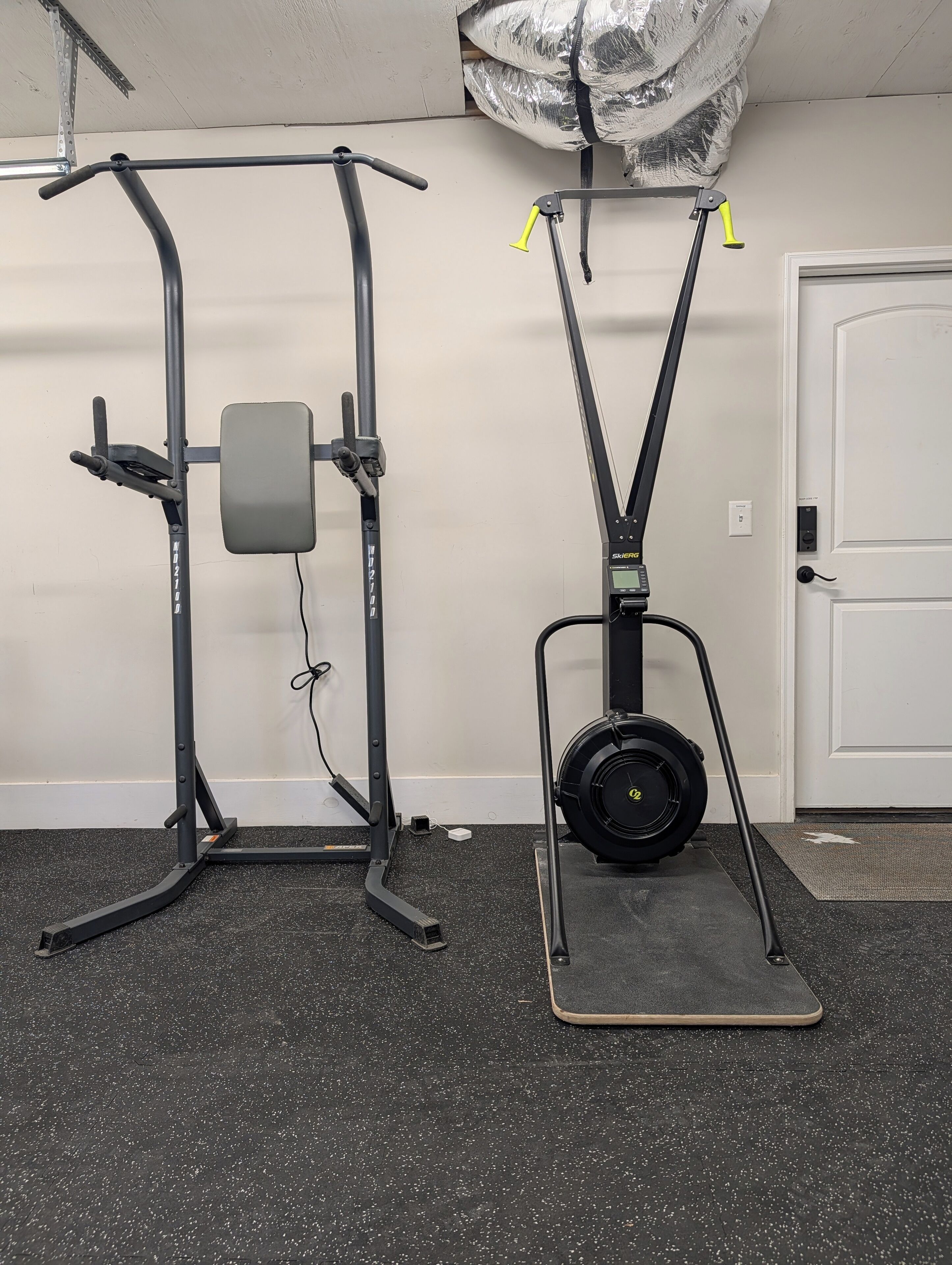 Two exercise machines in a room with a door and a wall socket.