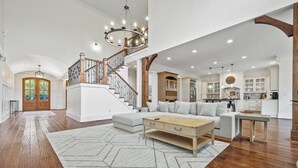 A spacious living room with a staircase, wooden flooring, and a large chandelier. - Buckhead Modern Luxury Home with Firepit & Arcade (Atlanta)