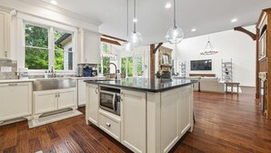 A spacious kitchen with white cabinetry, a large island, and a stone fireplace. - Buckhead Modern Luxury Home with Firepit & Arcade (Atlanta)
