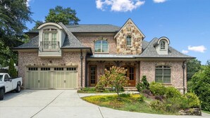 A two-story brick house with a garage, a front porch, and a small garden. - Buckhead Modern Luxury Home with Firepit & Arcade (Atlanta)