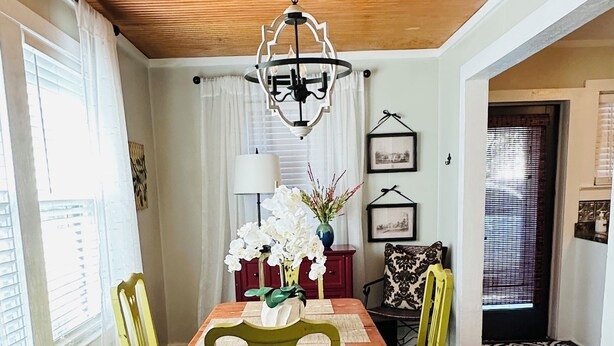 A dining area with a wooden ceiling, a chandelier, a table with chairs, and a floral rug.