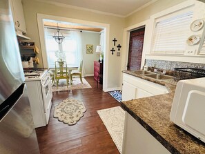 A kitchen with a gas stove, white cabinets, a dining area with a table and chairs, and a patterned rug.