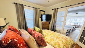 A bedroom with a bed, pillows, a dresser, a television, and a view of an outdoor patio.