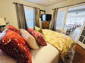 A bedroom with a bed, pillows, a dresser, a television, and a view of an outdoor patio.