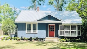 A single-story house with a red door, white shutters, and a grey roof.