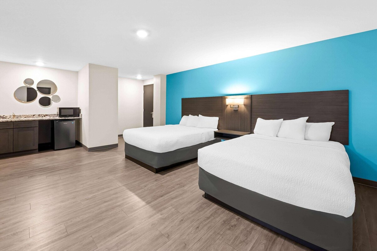 Une chambre d’hôtel avec deux lits, un coin cuisine et un mur d’accent bleu.