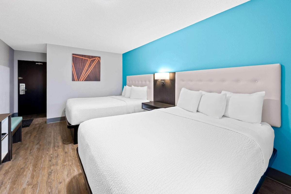 Habitación de hotel con dos camas, piso de madera, pared azul decorativa y lámpara moderna.