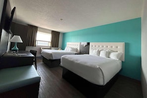 Quarto de hotel com duas camas, uma escrivaninha, uma cadeira, uma televisão e uma janela com cortinas.