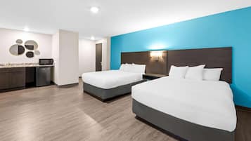 Habitación de hotel con dos camas, kitchenette y una pared azul de acento.