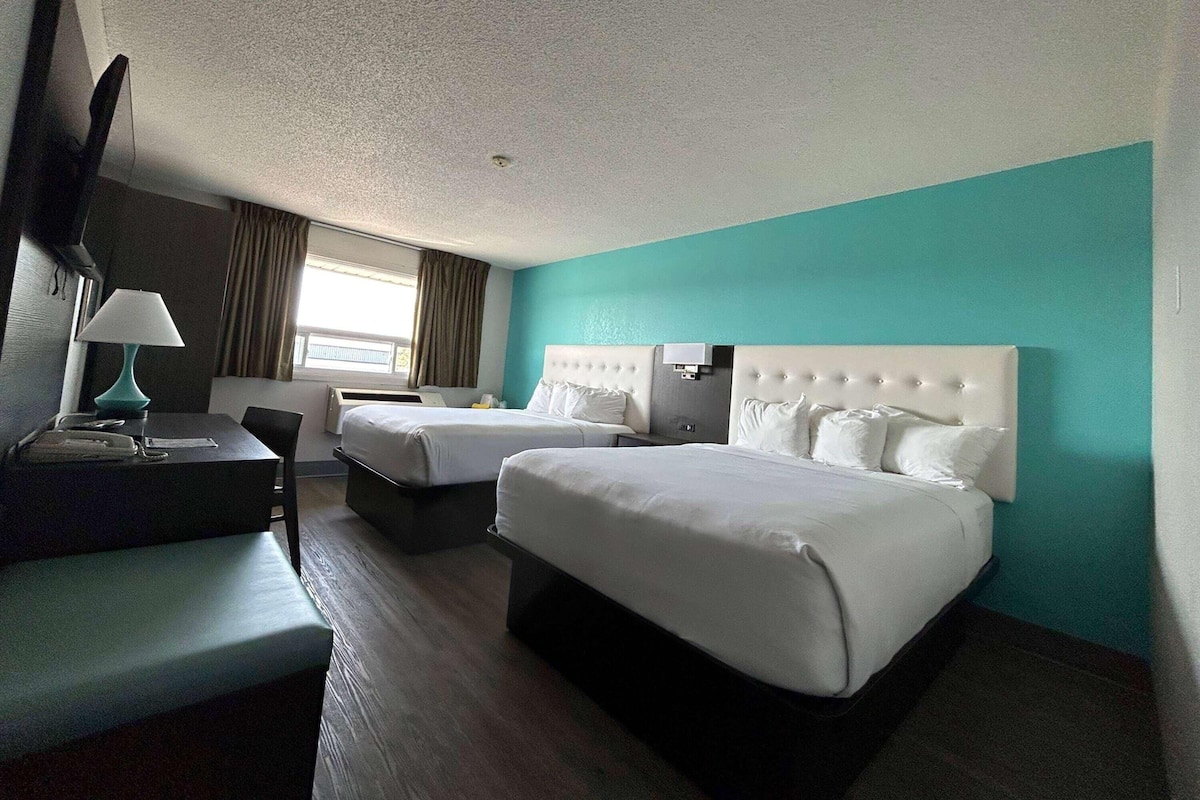 Habitación de hotel con dos camas, un escritorio, una silla, un televisor y una ventana con cortinas.