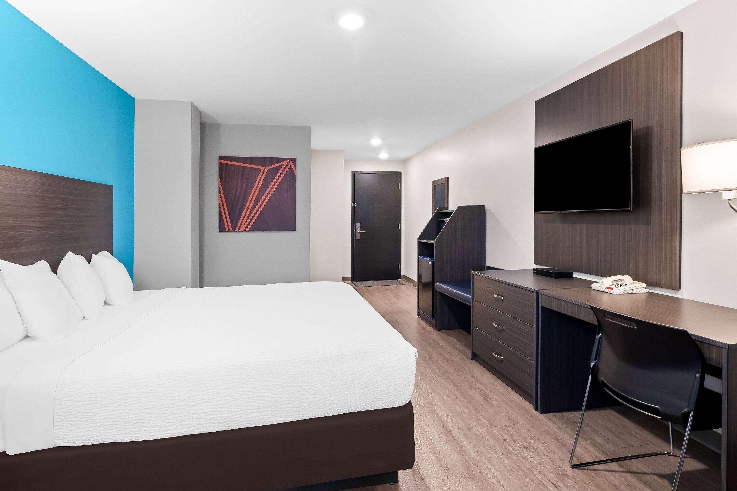 A hotel room with a bed, a desk, a television, and a door.