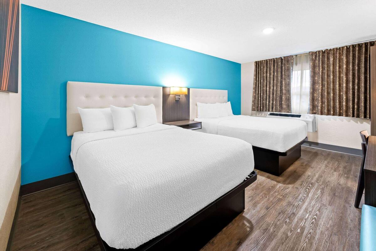 Una habitación de hotel con dos camas, un muro azul decorativo, suelo de madera y una ventana con cortinas.