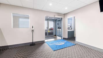 A hotel lobby with a reception desk, a blue mat with text, a window, and a door leading outside.