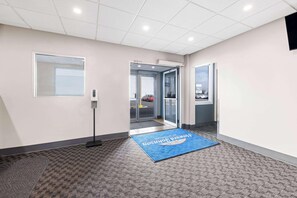 A hotel lobby with a reception desk, a blue mat with text, a window, and a door leading outside. - Howard Johnson by Wyndham Thunder Bay (Thunder Bay)